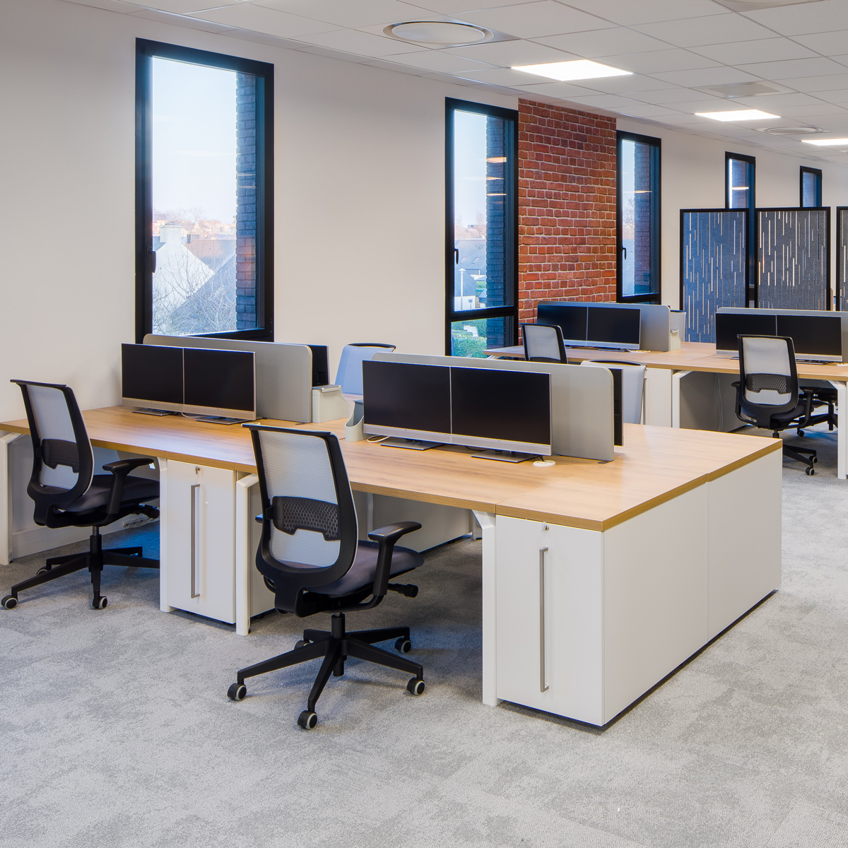 Desks with monitors and office chairs with large windows in the background